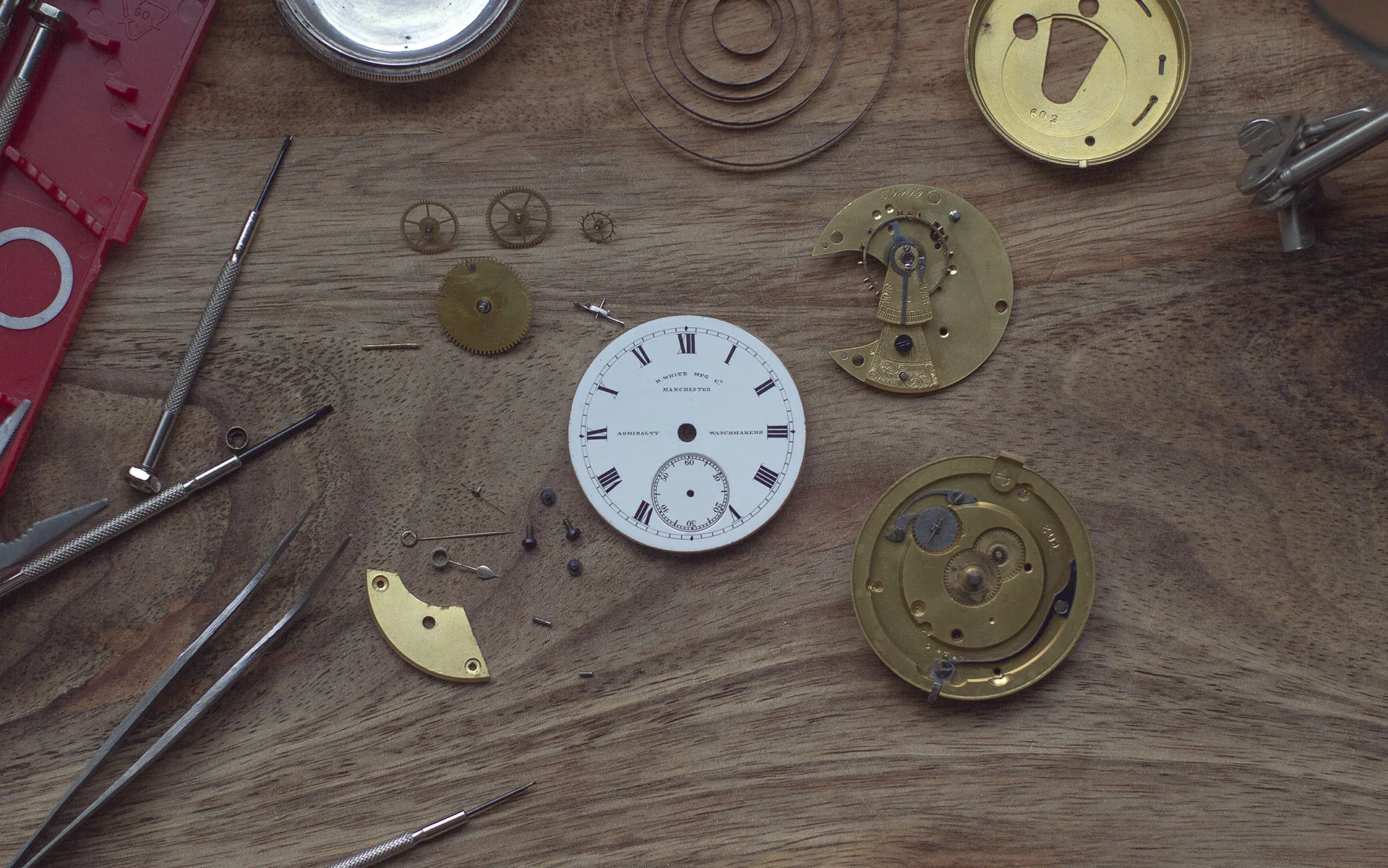 Pieces of a mechanical watch strewn on a wooden bench top.