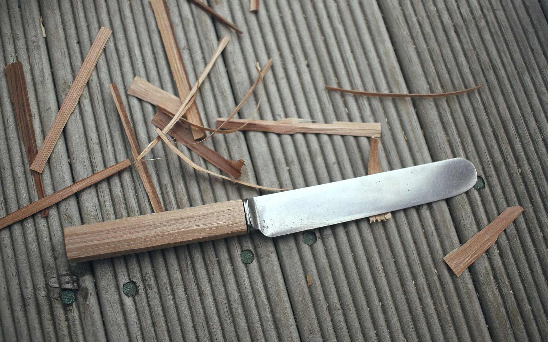 Knife with a rough cut of a new handle on a wooden surface with wood chips next to it.