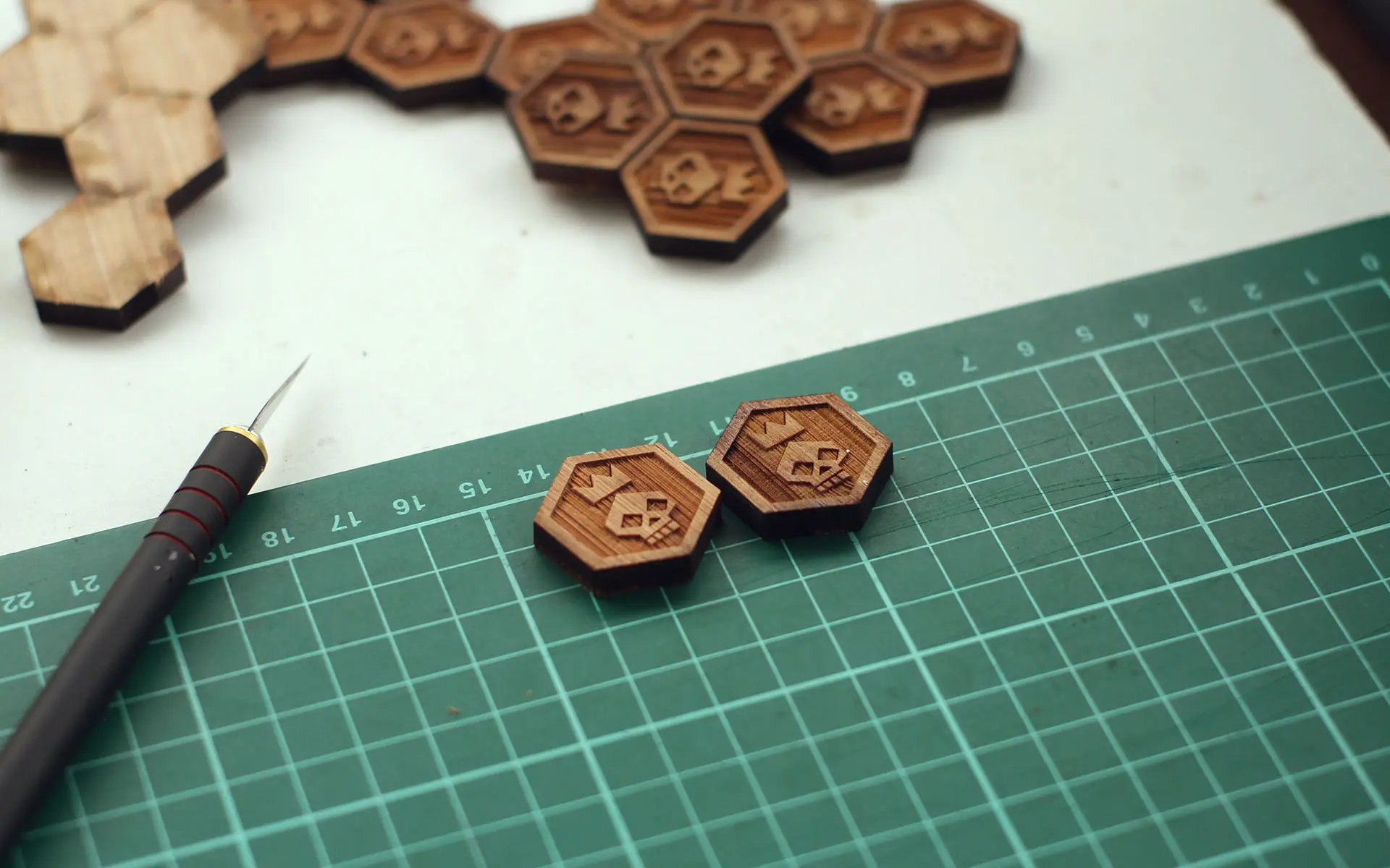 Two hexagonal pins with skulls and crowns sitting on a green cutting mat.