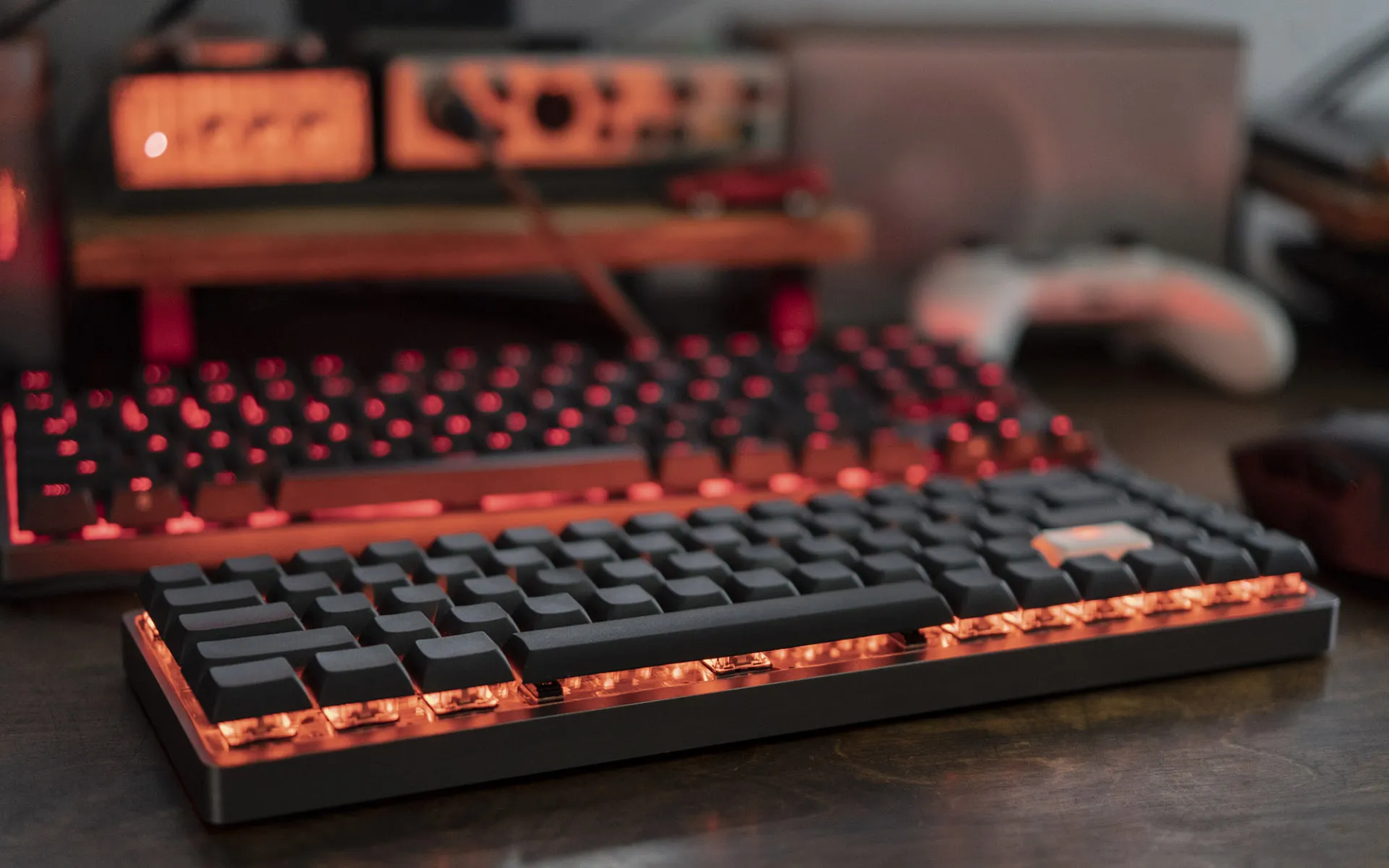 Black and charcoal keyboard with red underglow on a wooden desktop.
